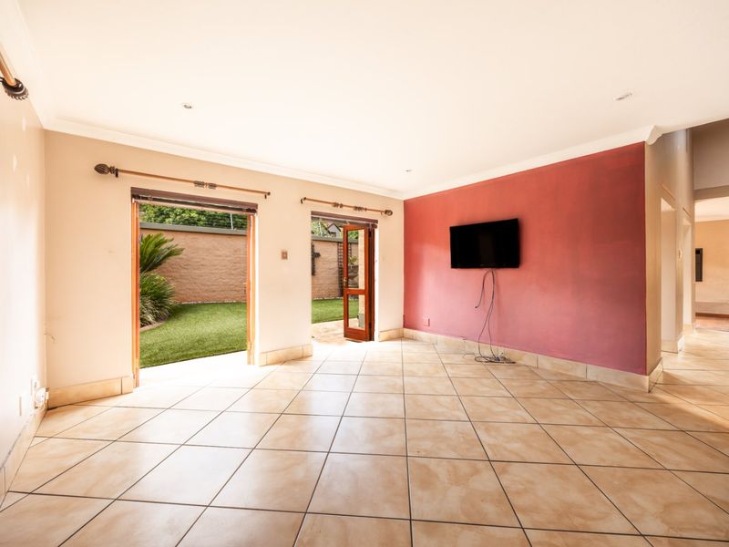 Spacious living area featuring ceramic floor tiles, an accent wall, and direct access to the rear garden through wooden doors.
