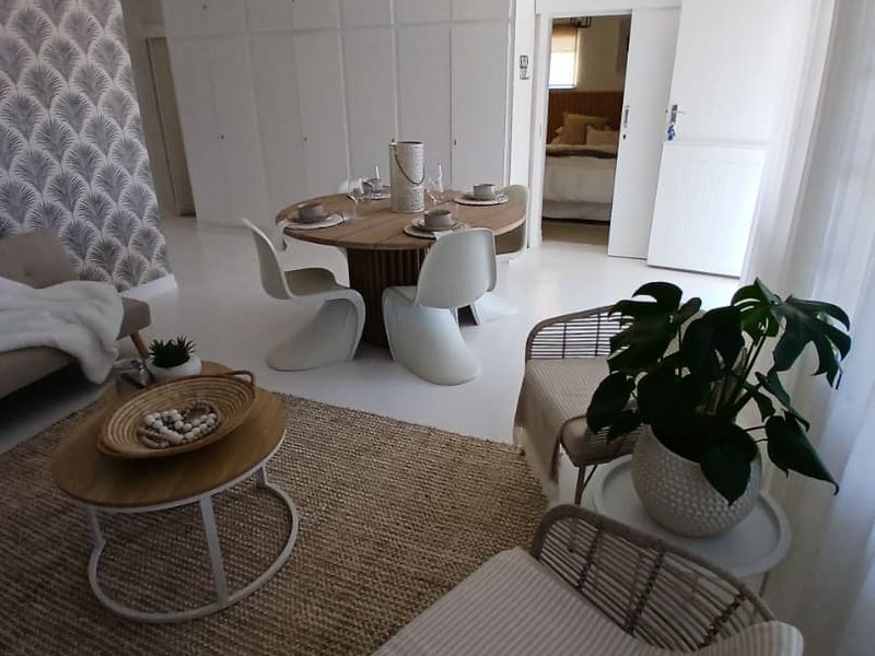 Bright open-plan living and dining area featuring built-in storage cupboards, neutral flooring, and direct access to an adjacent bedroom.