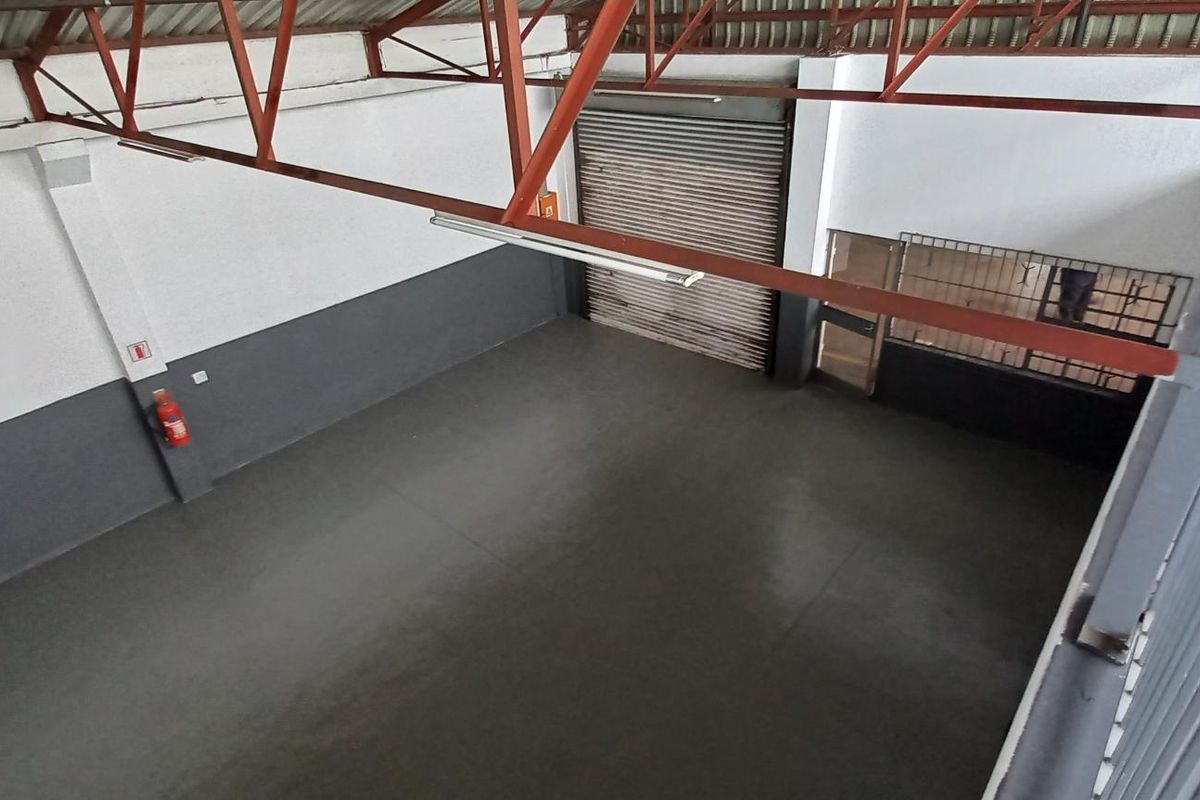 Spacious industrial utility area featuring high ceilings with exposed steel trusses, concrete flooring, and a secure roller shutter door access.