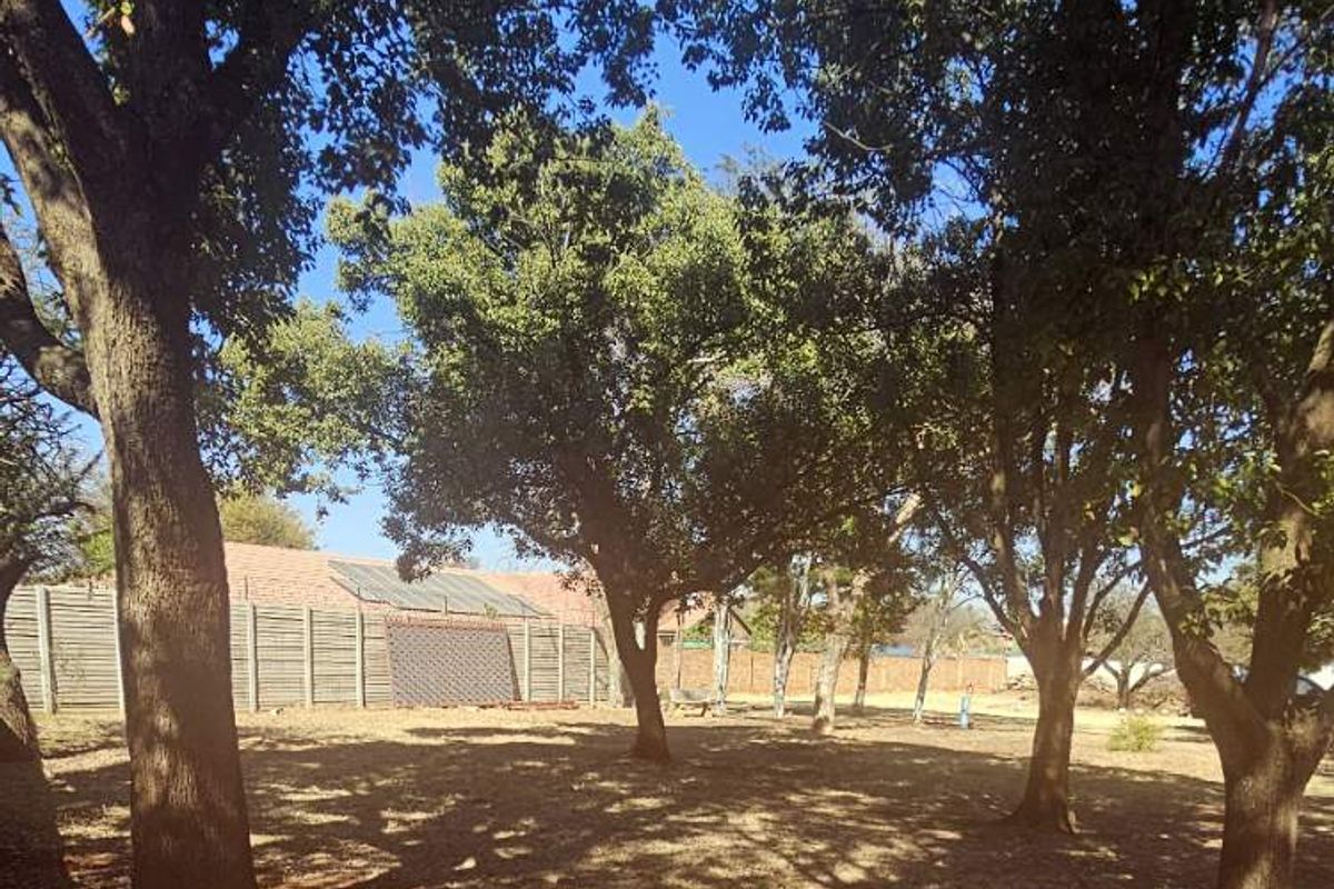 A spacious, tree-lined garden area featuring mature trees and a secure perimeter wall, offering a peaceful outdoor setting.