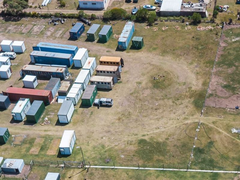 Aerial view of a large vacant residential plot featuring perimeter fencing and unpaved ground, currently utilized for storage of shipping containers.