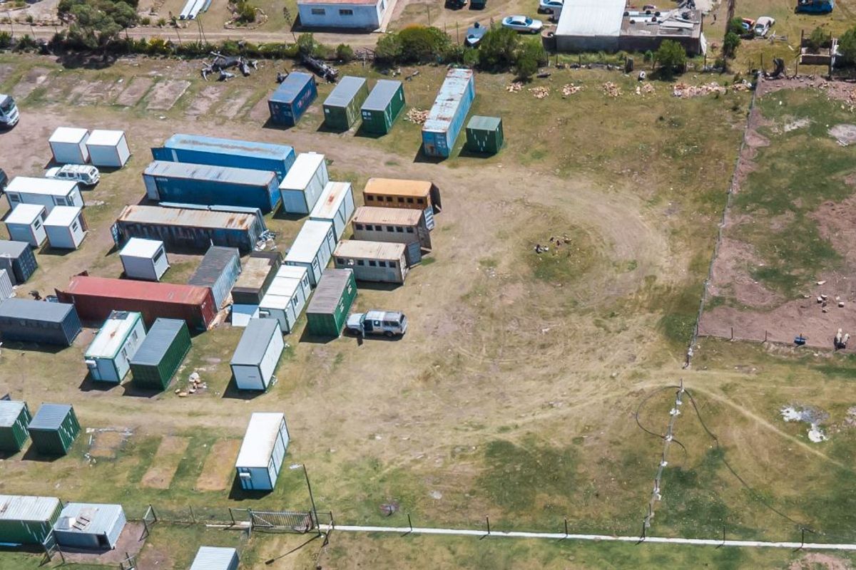 Aerial view of a large vacant residential plot featuring perimeter fencing and unpaved ground, currently utilized for storage of shipping containers.