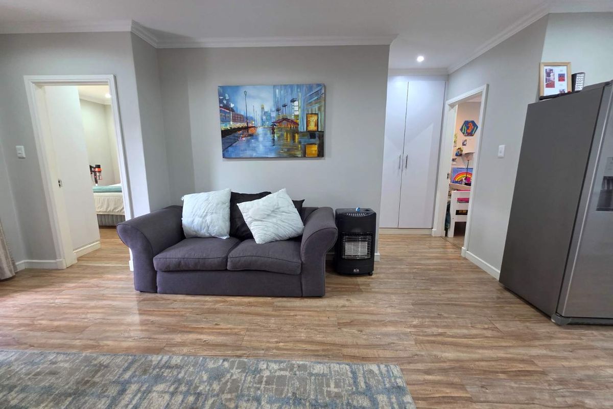 A living area featuring wood-look flooring, built-in cupboards, and access to adjacent rooms, providing a functional and neutral living space.