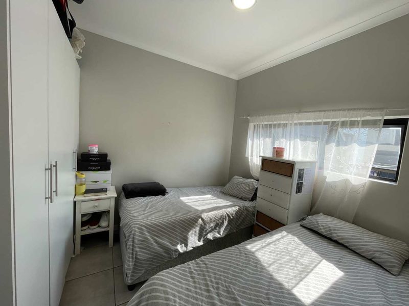 A functional bedroom featuring tiled flooring, a built-in wardrobe, and natural light through a window with sheer curtains.