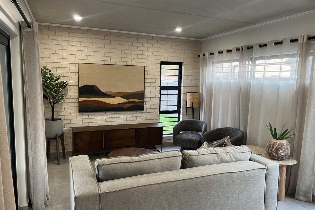 A well-lit living room featuring a textured white brick accent wall, tiled flooring, and large windows with modern curtain treatments.