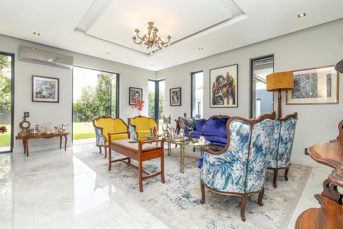 Spacious living room featuring polished marble flooring, recessed tray ceiling with chandelier, and large glass sliding doors providing seamless access to the garden.