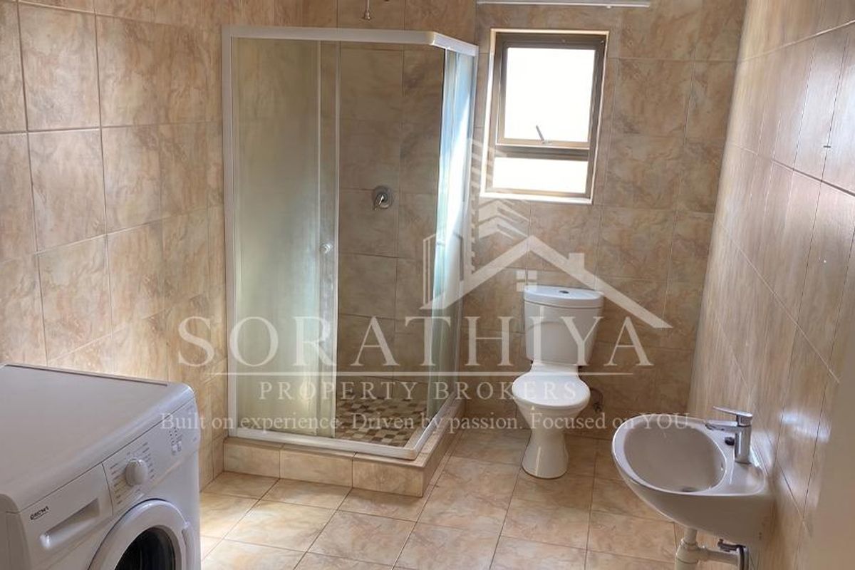 A functional bathroom featuring a shower enclosure, toilet, and wall-mounted basin with neutral wall and floor tiling.