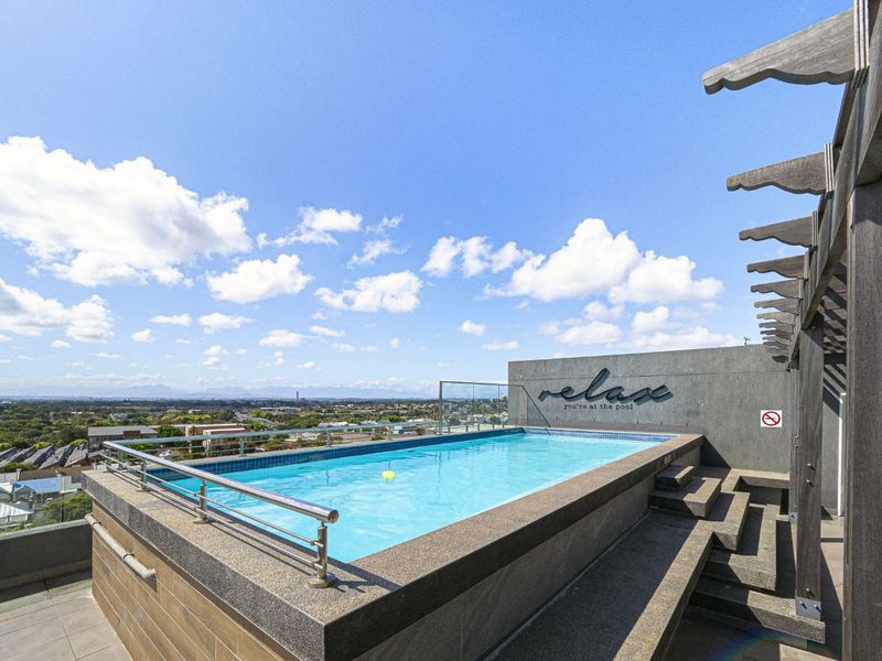 A well-maintained rooftop swimming pool featuring a glass balustrade, stainless steel handrail, and panoramic city views.