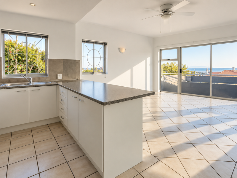 Bright open-plan kitchen and living area featuring tiled floors, a functional kitchen island, and large sliding doors leading to a balcony with scenic views.