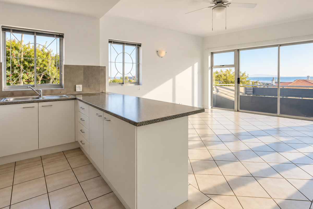 Bright open-plan kitchen and living area featuring tiled floors, a functional kitchen island, and large sliding doors leading to a balcony with scenic views.