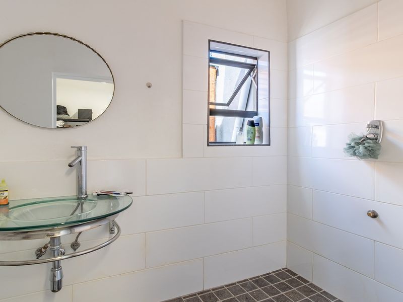 A clean, modern bathroom featuring a glass vessel sink, chrome fixtures, and white wall tiling with a dark tiled floor.