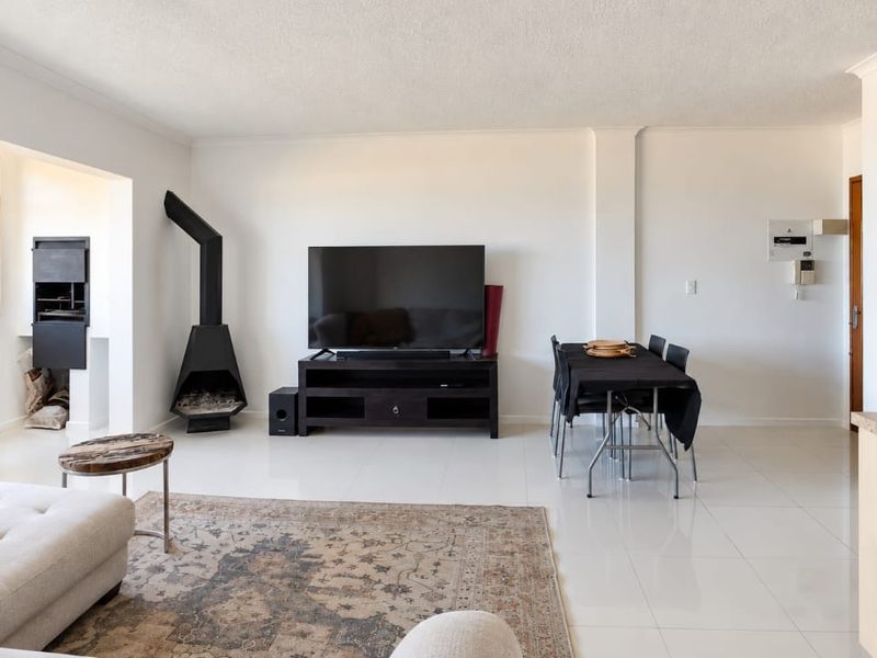 Spacious open-plan living and dining area featuring tiled floors, a built-in fireplace, and a built-in braai with scenic coastal views.