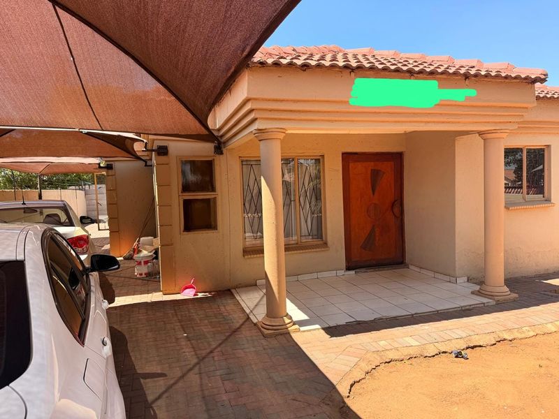 Front entrance of the house featuring a tiled porch with decorative columns, a paved driveway, and a shade sail structure for vehicle protection.