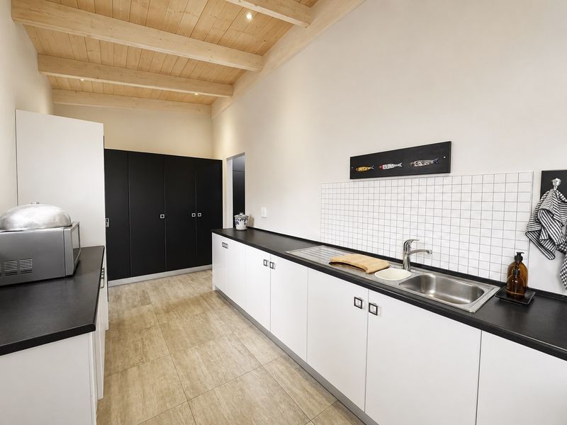 A modern, well-maintained scullery featuring sleek white and black cabinetry, a stainless steel sink, tiled splashback, and an attractive exposed timber beam ceiling.