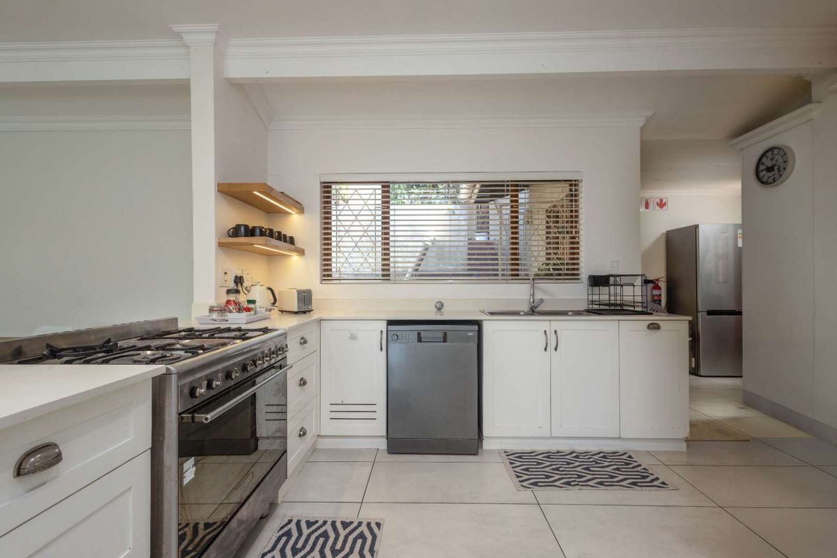 A functional kitchen featuring white cabinetry, stone countertops, a gas stove with oven, integrated dishwasher, and floating timber shelving with under-cabinet lighting.