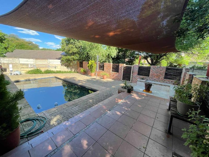 Outdoor entertainment area featuring a swimming pool, brick-paved patio, built-in seating, and a shade sail, enclosed by a brick boundary wall.
