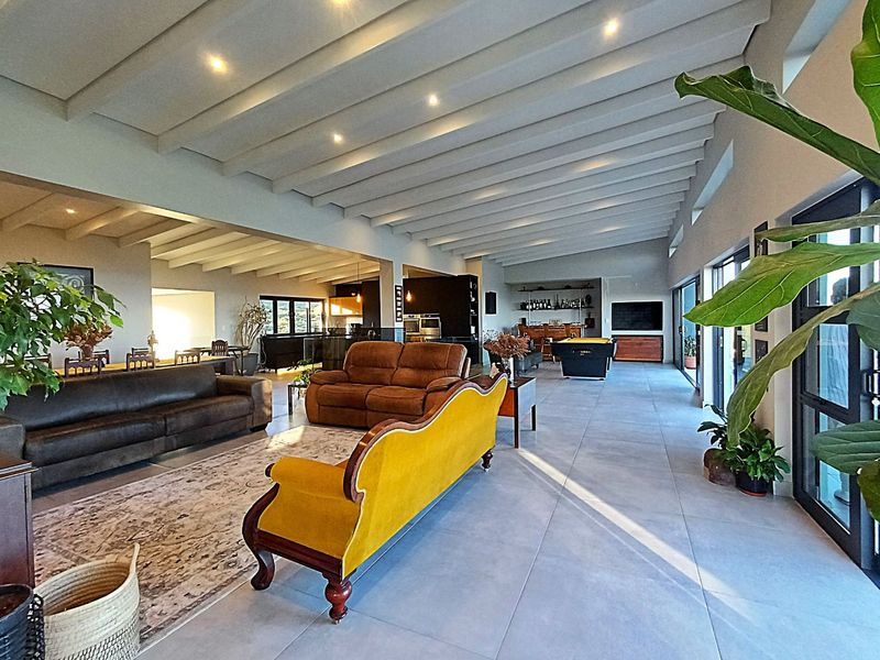 Spacious open-plan living area featuring high exposed beam ceilings, large format floor tiles, and seamless flow to the outdoor area through sliding glass doors.
