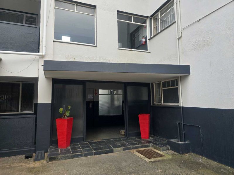 The apartment building entrance features a tiled step area, sliding glass doors, and metal-framed windows with a functional exterior design.