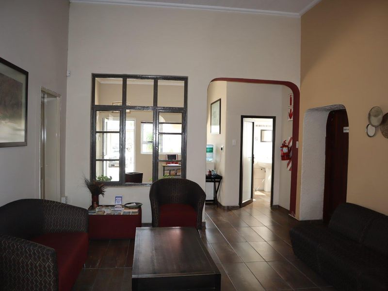 A reception or waiting area in an office space featuring tiled flooring, an internal window, and an arched doorway leading to further office facilities.