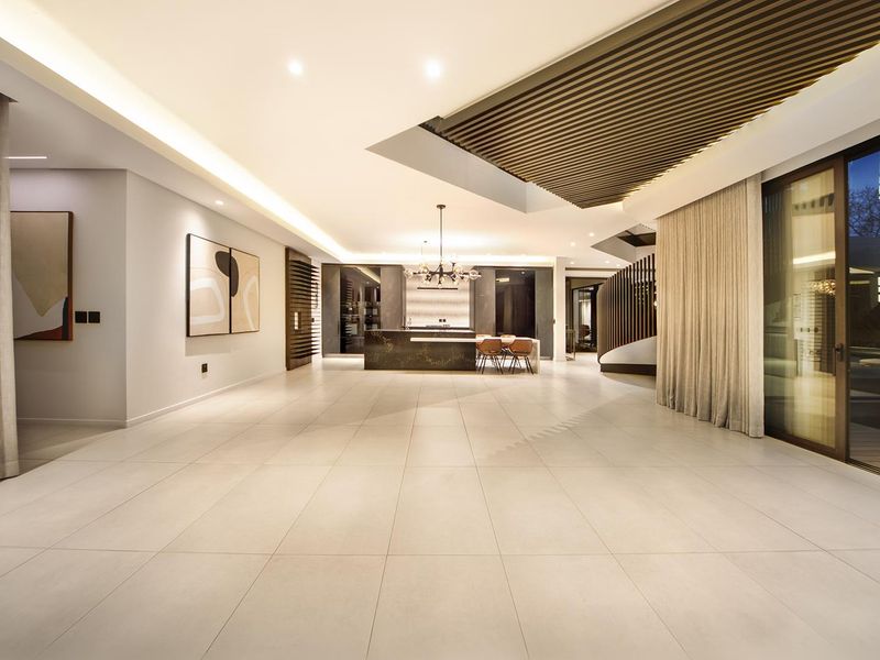 Spacious open-plan living and kitchen area featuring large format floor tiles, recessed lighting, a slatted timber ceiling detail, and expansive sliding glass doors.