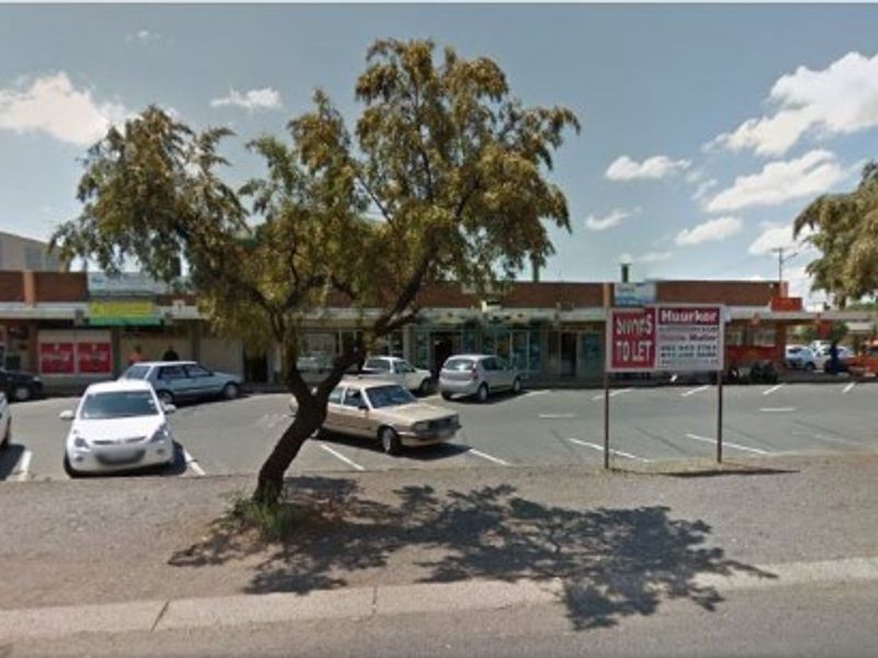 Street view of a commercial strip mall with an asphalt parking area and storefronts.