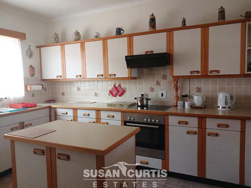 A functional kitchen featuring dated cabinetry, laminate countertops, a tiled backsplash, and a central island, providing a practical layout for daily meal preparation.