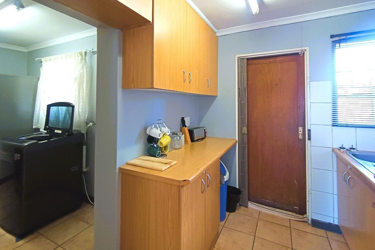 A functional kitchen area featuring wood-look cabinetry, tiled flooring, and a direct access door, providing a practical layout for daily utility.