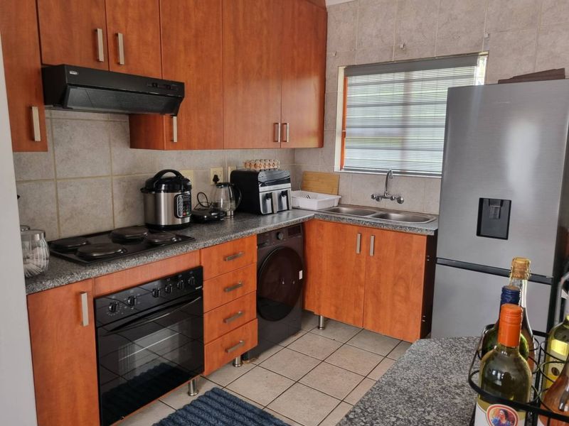 A functional kitchen featuring wooden cabinetry, granite countertops, a built-in oven with hob, and a double stainless steel sink with tiled finishes.