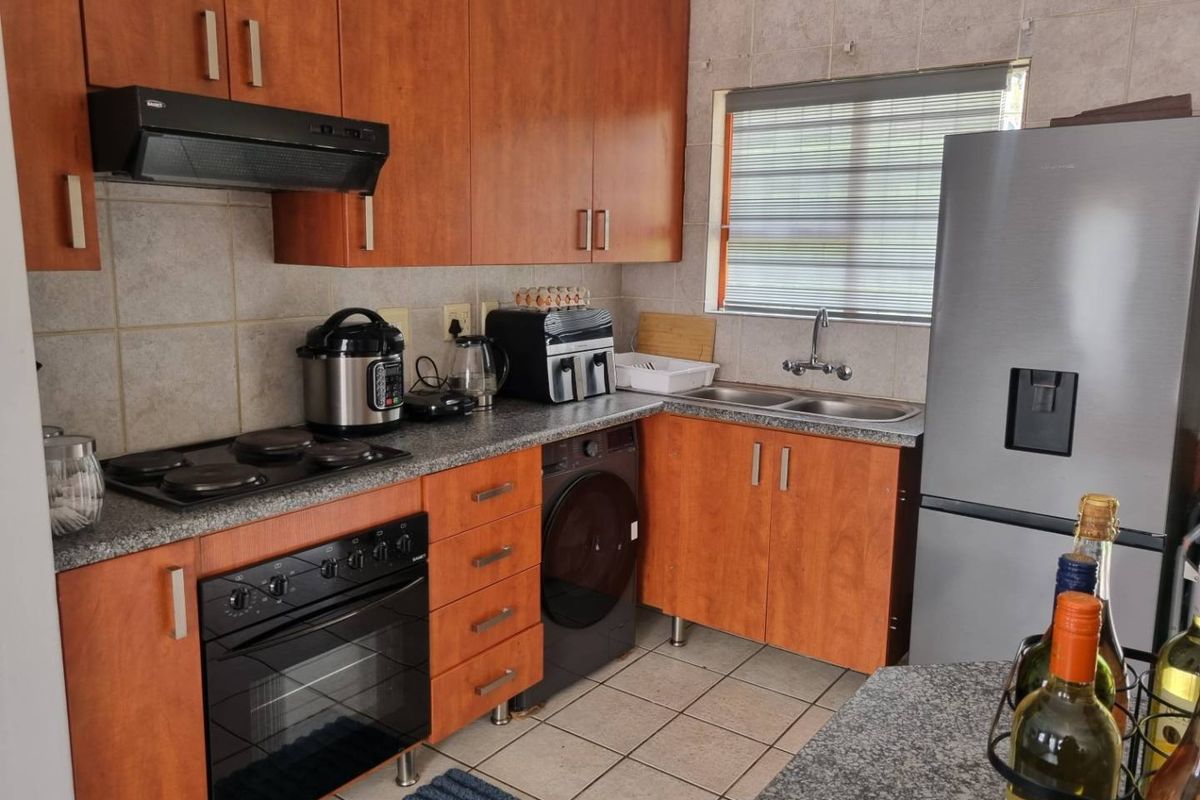 A functional kitchen featuring wooden cabinetry, granite countertops, a built-in oven with hob, and a double stainless steel sink with tiled finishes.