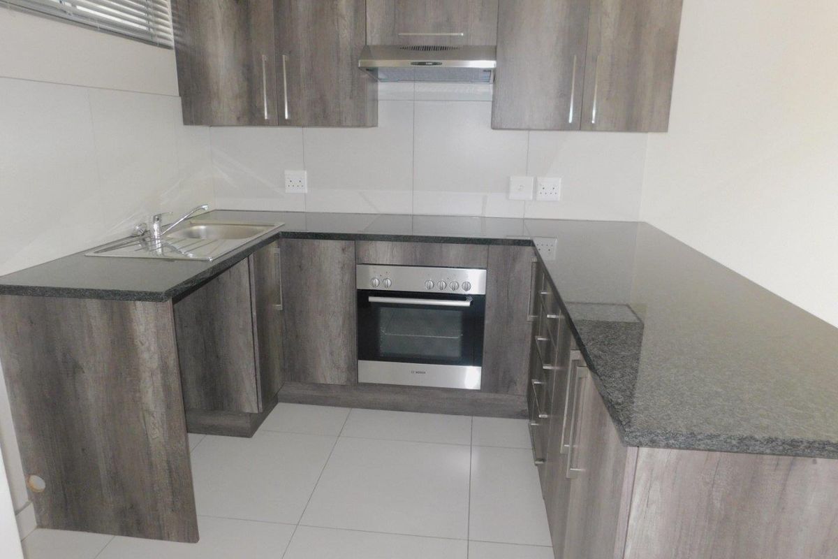 Modern kitchen featuring dark wood-grain cabinetry, granite countertops, stainless steel oven, extractor fan, and clean tiled finishes.