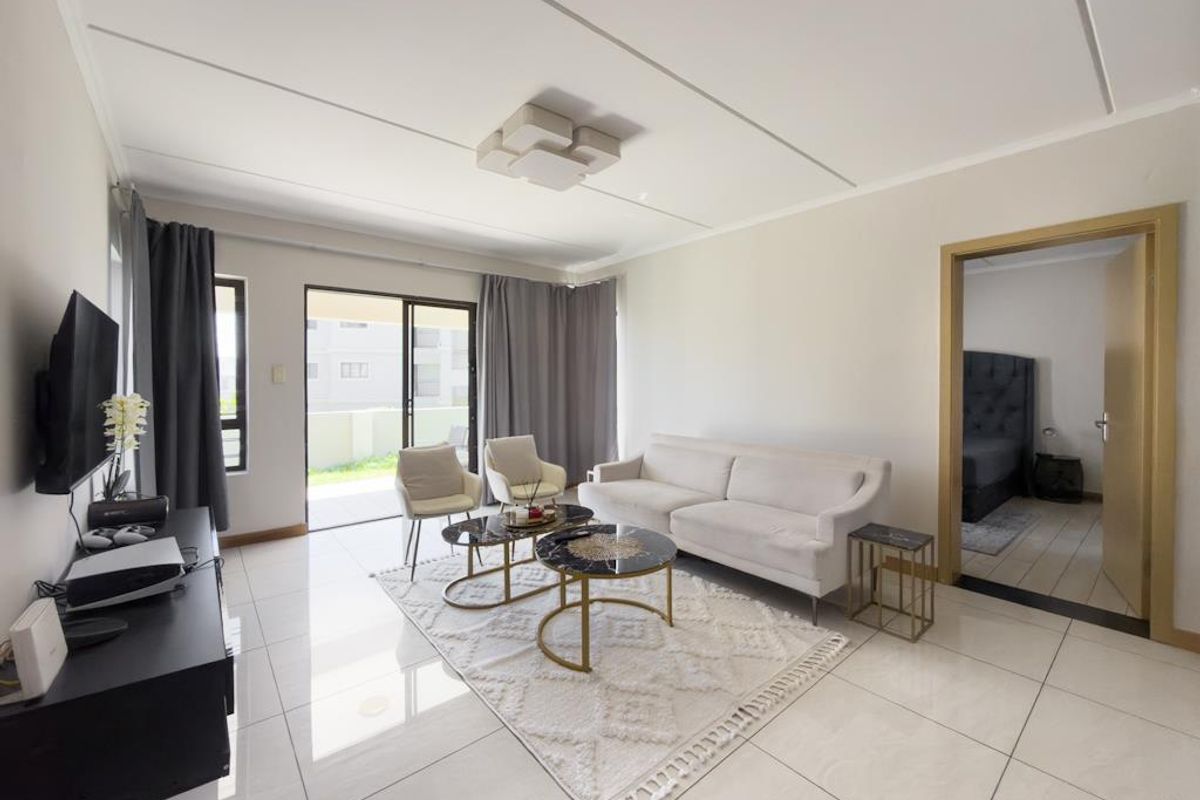 A bright and spacious living room featuring large format floor tiles, a modern ceiling light fixture, and sliding glass doors leading to a private balcony.