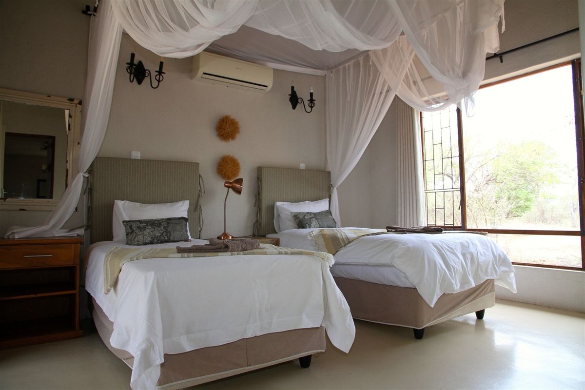 A spacious bedroom featuring a split-system air conditioner, large window with security bars, and neutral wall finishes.