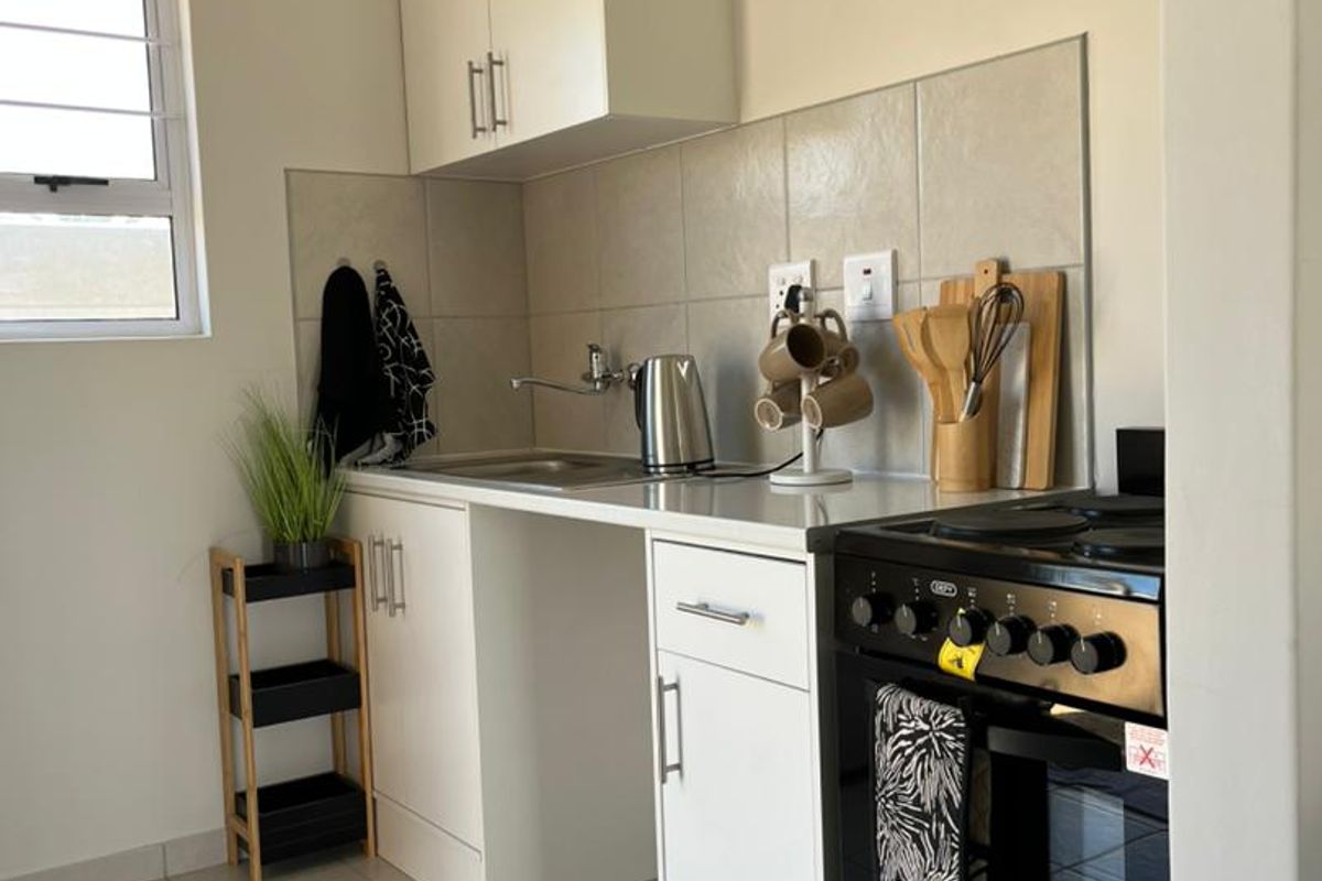 A compact, well-maintained kitchen featuring white cabinetry, tiled backsplash, stainless steel sink, and a modern freestanding oven.