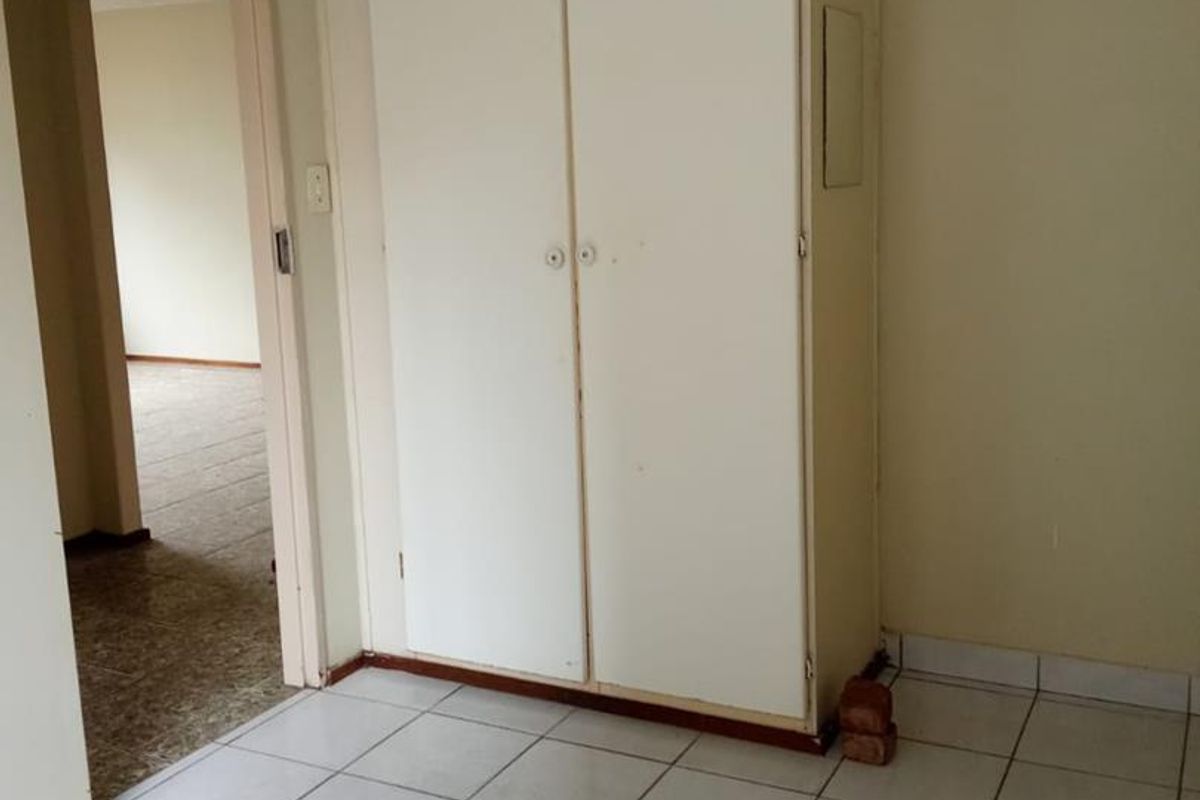 An empty bedroom featuring white ceramic floor tiles and a built-in cupboard with visible wear at the base.