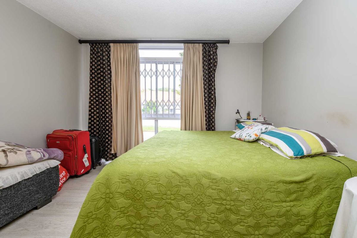 A functional bedroom featuring laminate flooring and a window fitted with a security gate, providing a practical and secure living space.