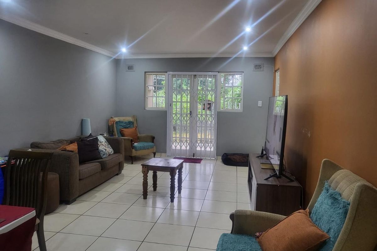 Spacious living room featuring ceramic tiled flooring, recessed downlighting, crown molding, and a secure sliding glass door leading to the exterior.