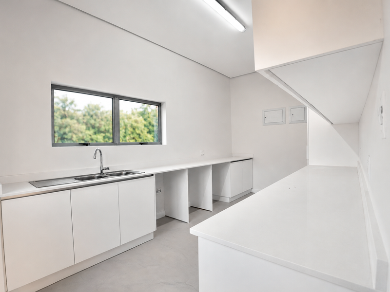 A clean, modern, and empty scullery featuring white cabinetry, stone countertops, a stainless steel sink, and ample workspace.