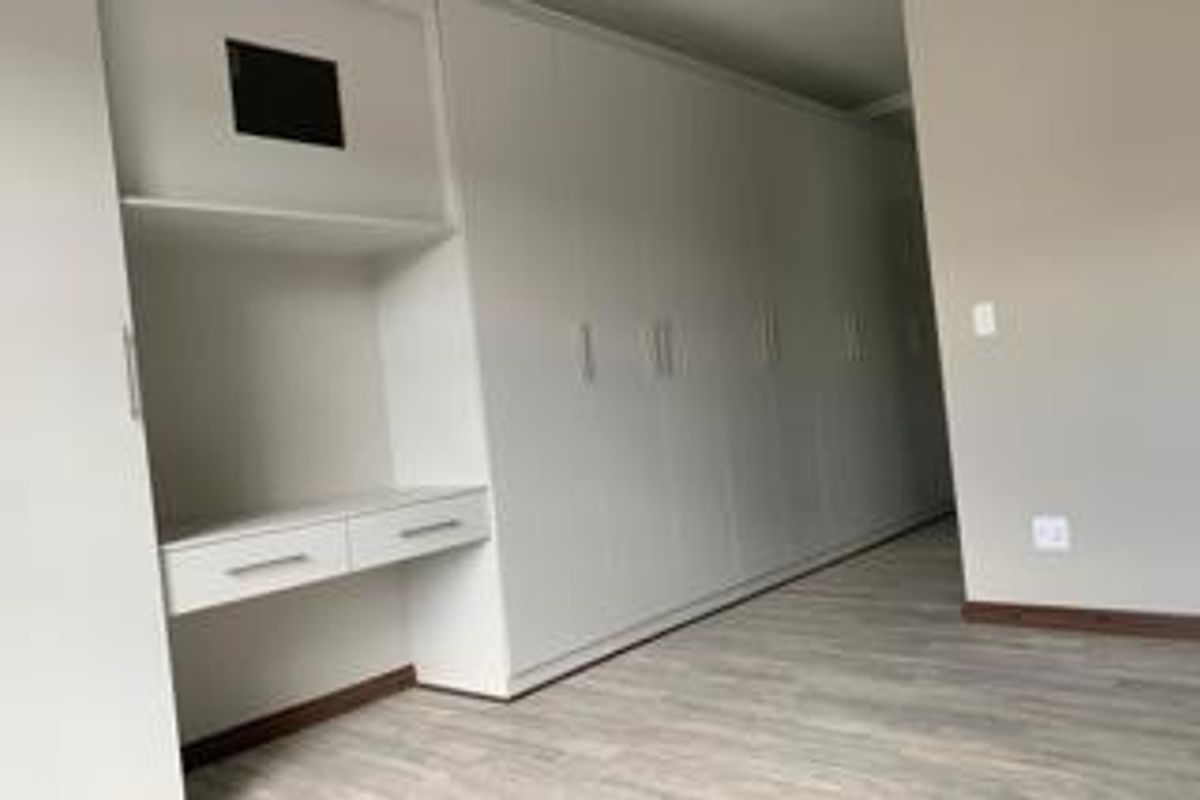 A clean, modern bedroom featuring extensive white built-in cupboards, a integrated desk area, and light-toned laminate flooring.