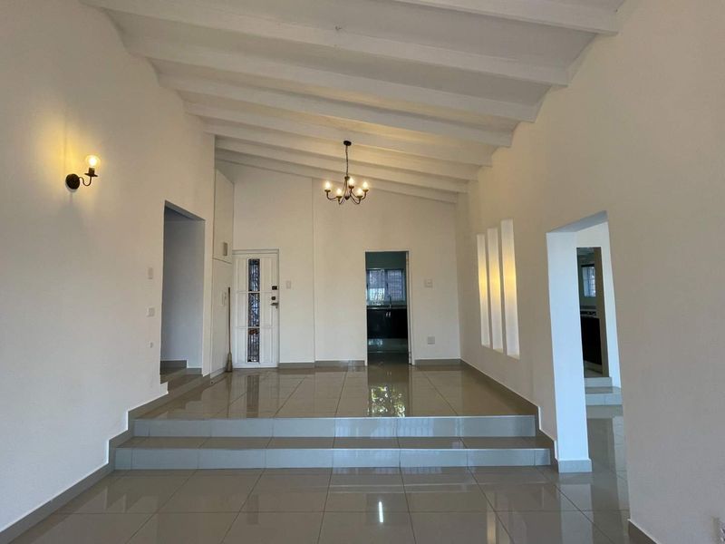 Spacious living area featuring a raised platform, high exposed beam ceilings, tiled flooring, and elegant lighting fixtures, offering a bright and open layout.