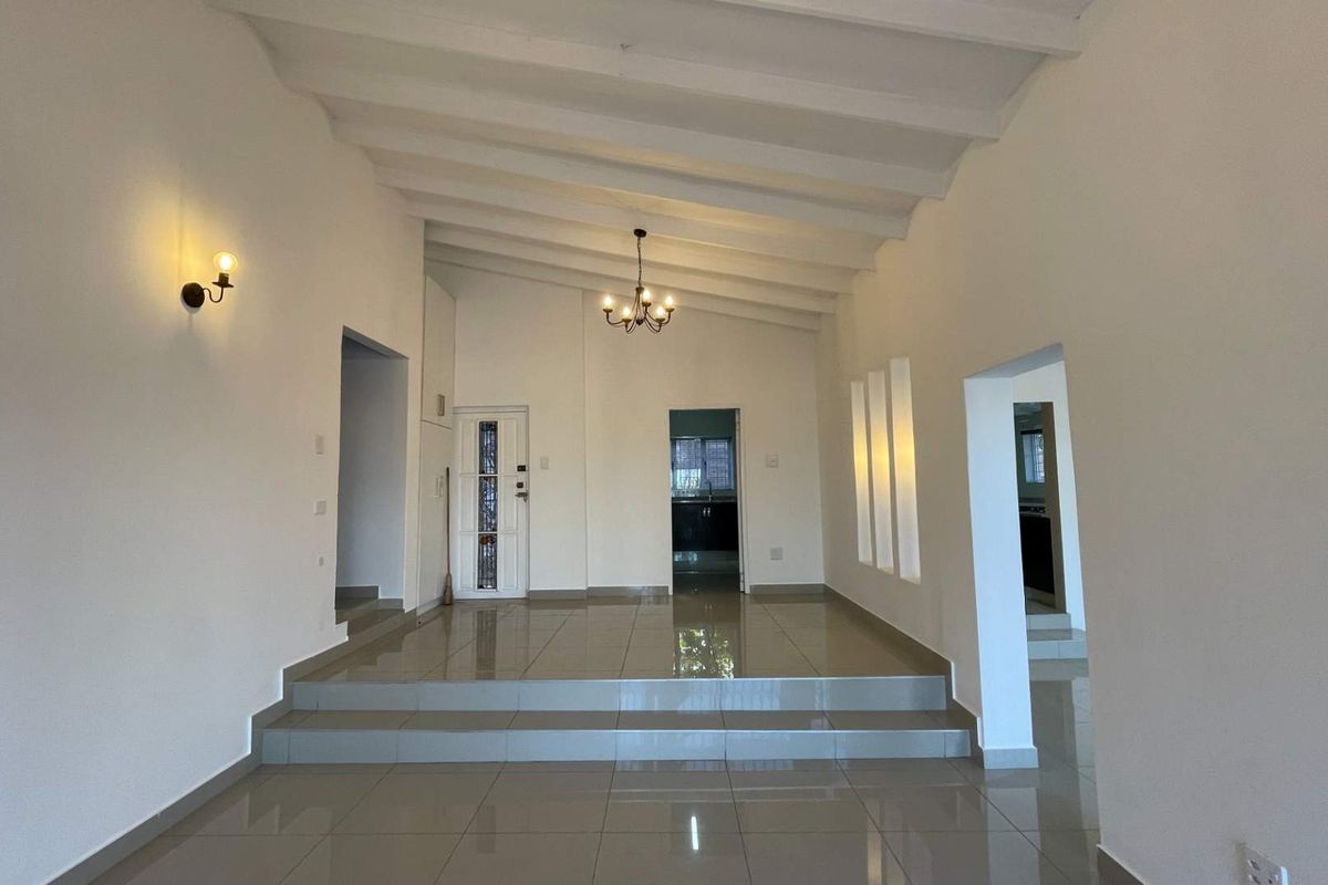 Spacious living area featuring a raised platform, high exposed beam ceilings, tiled flooring, and elegant lighting fixtures, offering a bright and open layout.