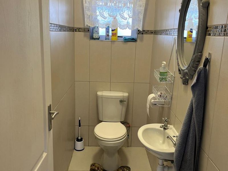 A compact guest bathroom featuring tiled walls and flooring, a standard toilet, and a wall-mounted basin.