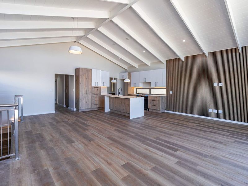Spacious open-plan living area featuring a modern kitchen with island, vaulted ceilings with exposed beams, and a contemporary slatted wood feature wall.