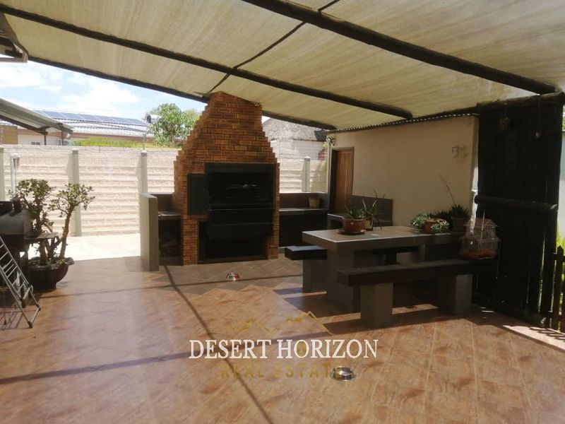 Covered outdoor patio area featuring a built-in brick braai, tiled flooring, and integrated concrete seating, ideal for outdoor entertaining.