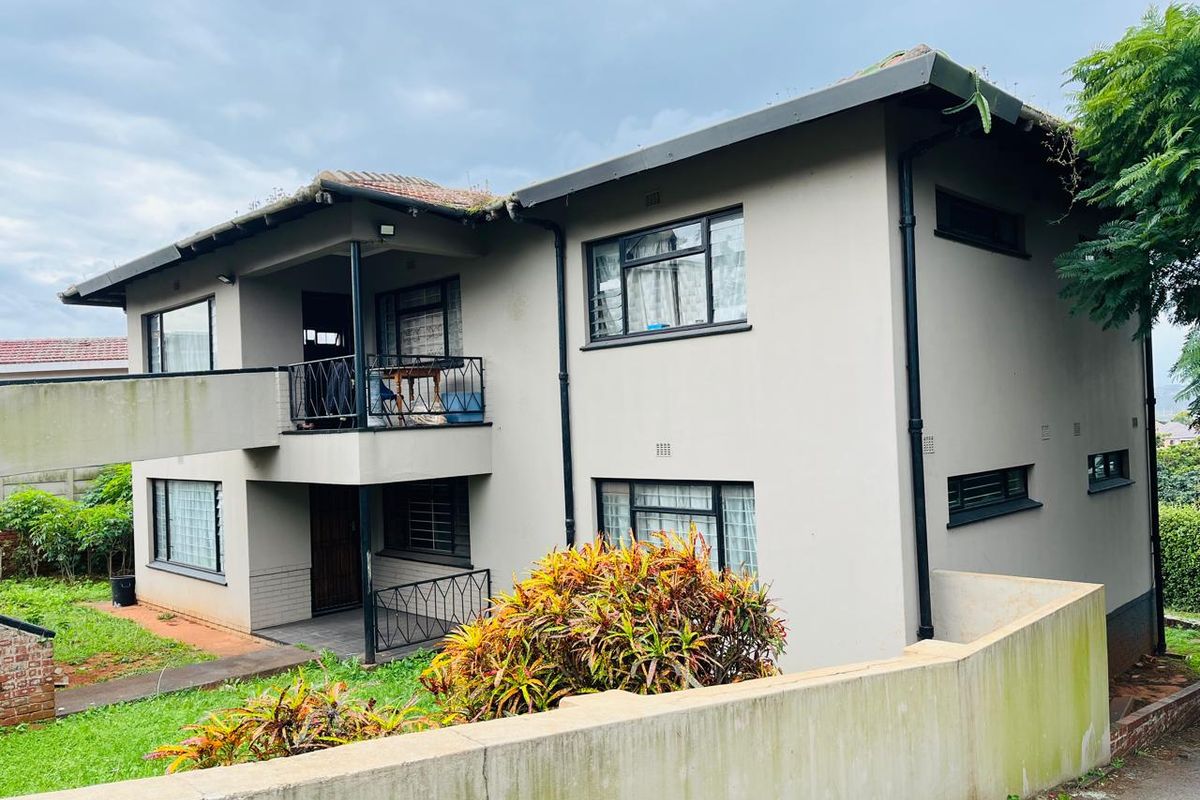 Rear view of a two-story residential building featuring a balcony with wrought iron railings and a concrete boundary wall.