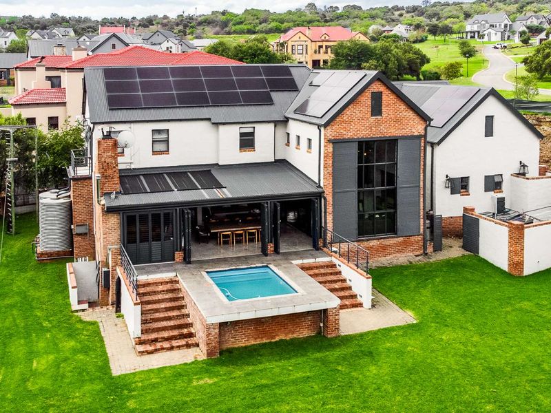 Aerial view of a modern brick and plaster home featuring a swimming pool, covered patio, and extensive rooftop solar panel installation.