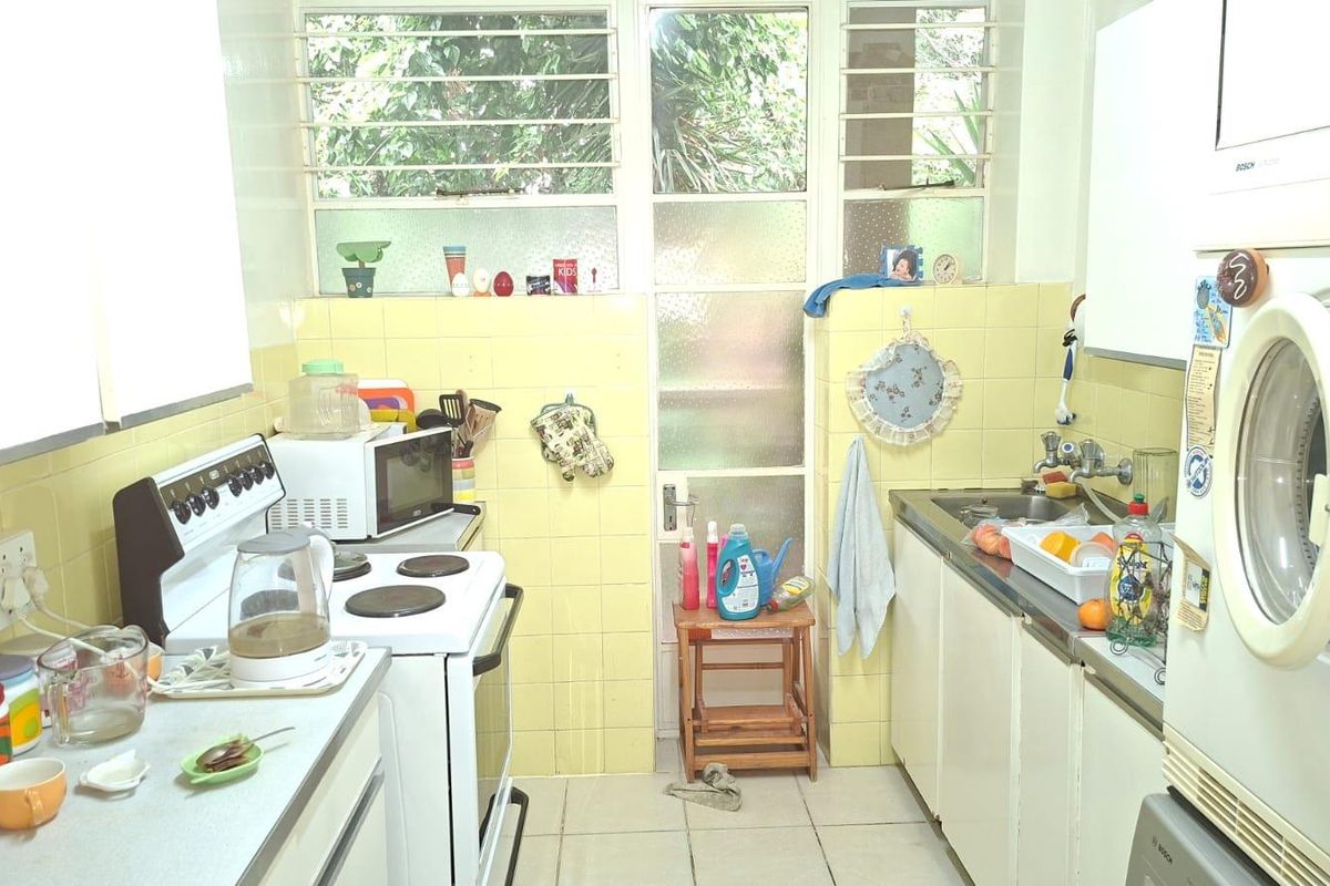 A functional kitchen featuring tiled splashbacks, built-in cabinetry, a stainless steel sink, and a freestanding stove, with louvered windows providing natural light.