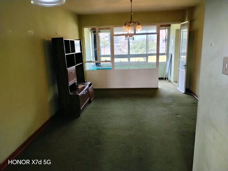 A spacious living area featuring large windows, carpet flooring, and a ceiling light fixture, offering a blank canvas for renovation and modernization.