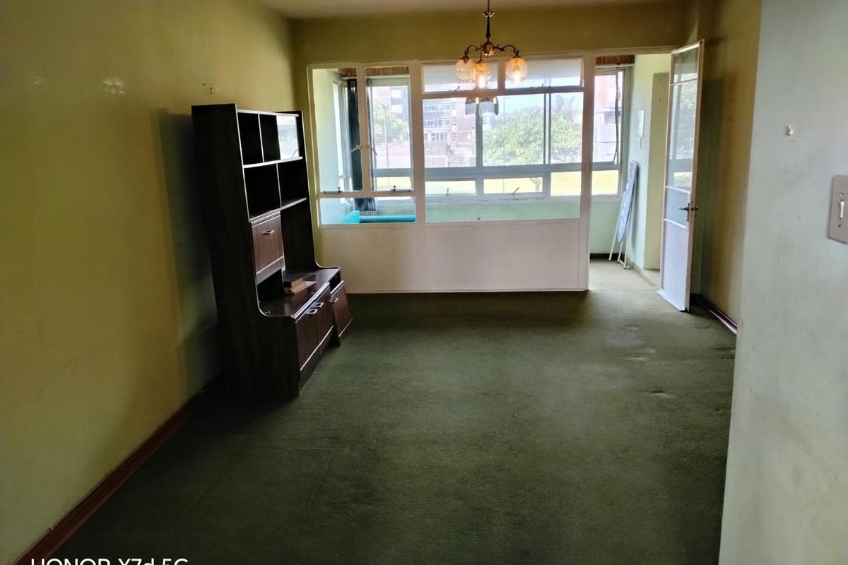 A spacious living area featuring large windows, carpet flooring, and a ceiling light fixture, offering a blank canvas for renovation and modernization.