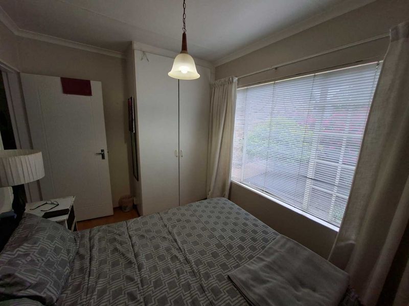 A functional bedroom featuring built-in wardrobes, laminate flooring, and large windows with venetian blinds, providing natural light and storage space.