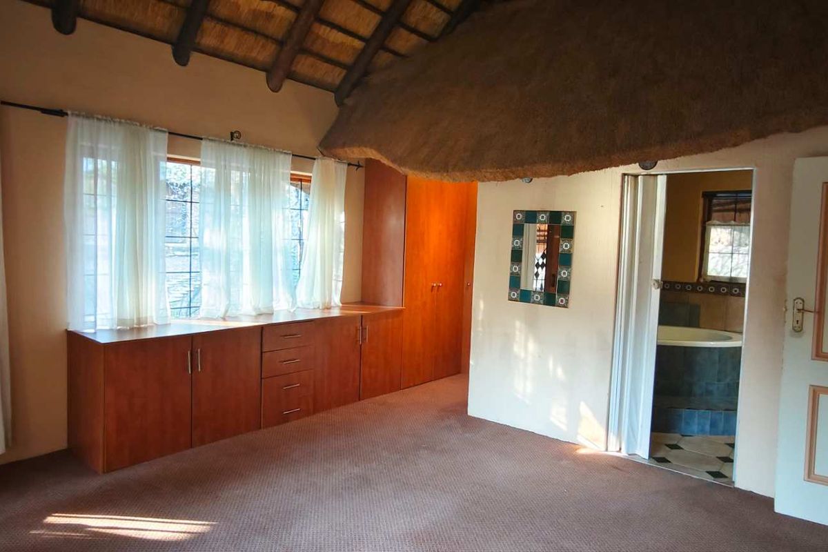 Spacious bedroom featuring a unique thatched roof ceiling, built-in wooden cabinetry, and an en-suite bathroom access.